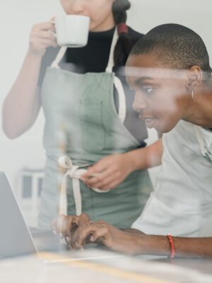 Black female barista together with colleague using laptop at work