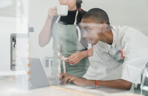 Black female barista together with colleague using laptop at work