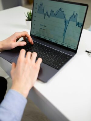 Crop unrecognizable male entrepreneur typing on laptop keyboard while preparing financial diagrams during work in office